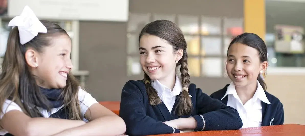 Tres estudiantes sonriendo juntas en el aula durante una clase en el colegio